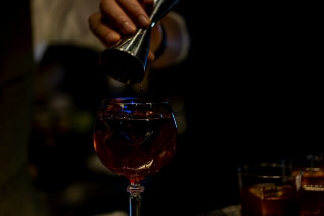 Dark image of hand holding a shot glass pouring alcohol into a glass to create a cocktail