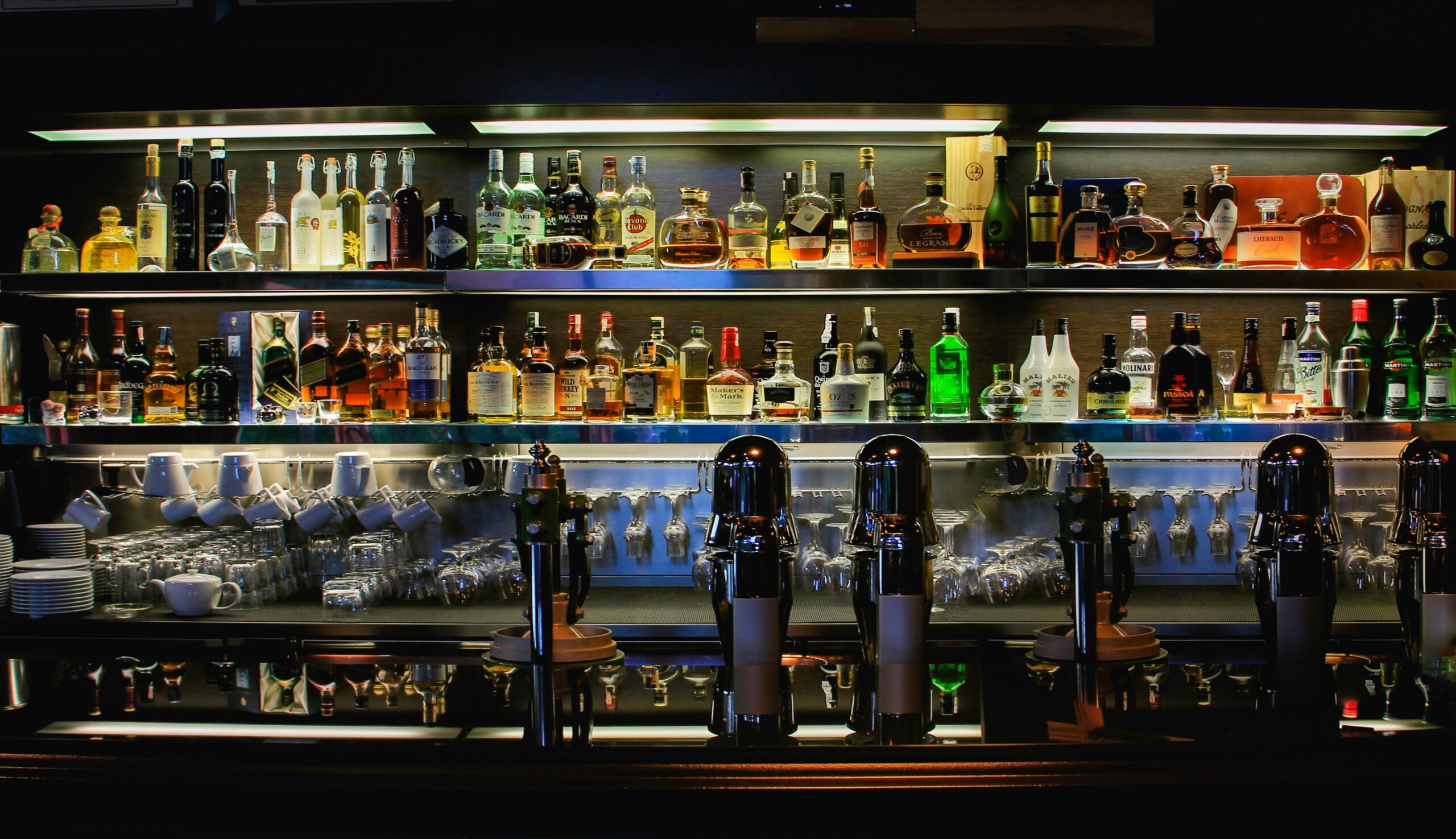 A dimly lit bar with shelves stacked with bottles of alcohol, glasses and beer dispensers