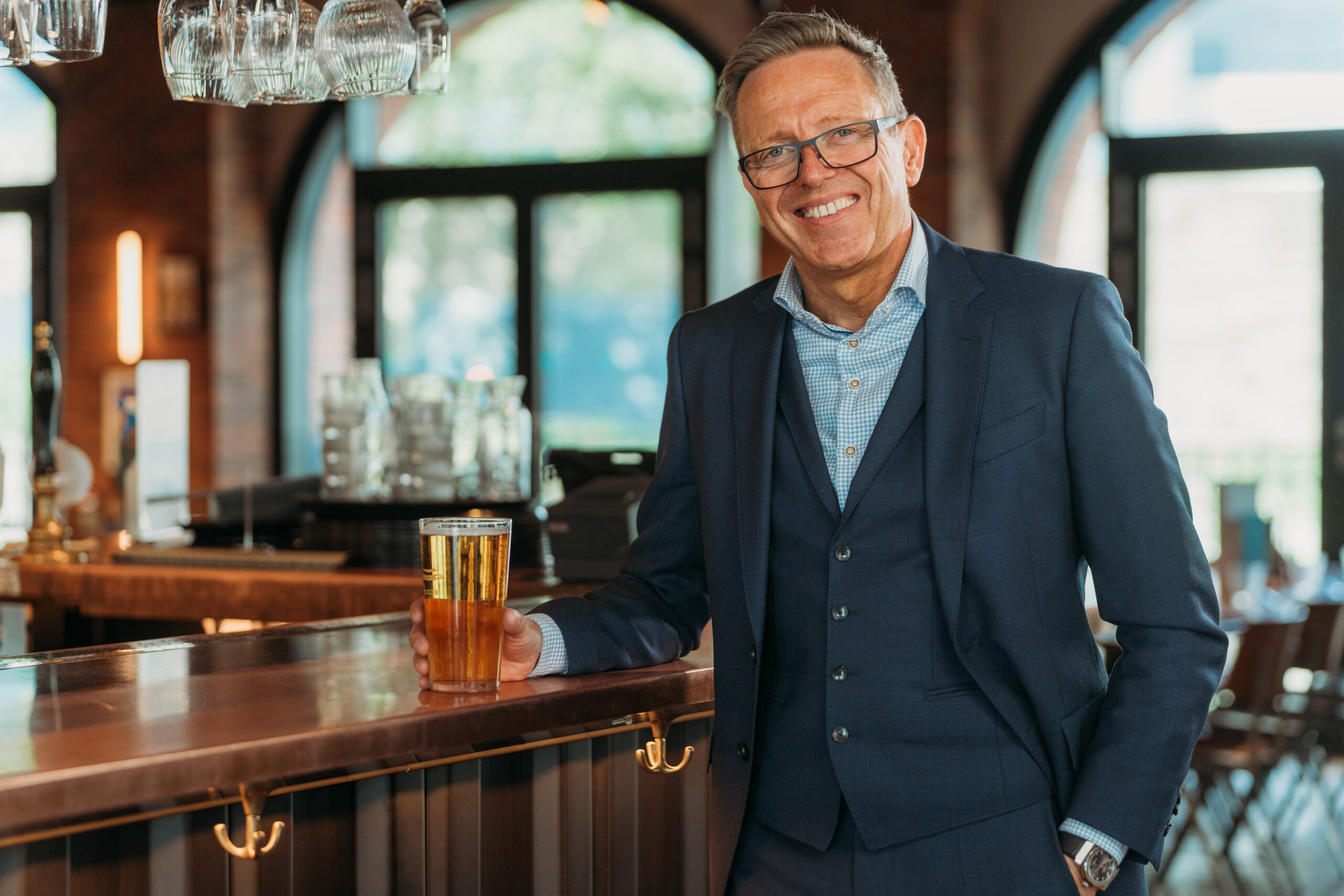 Managing Partner, Graeme Cushion, smiling into camera holding a pint of beer. Wearing a navy suit